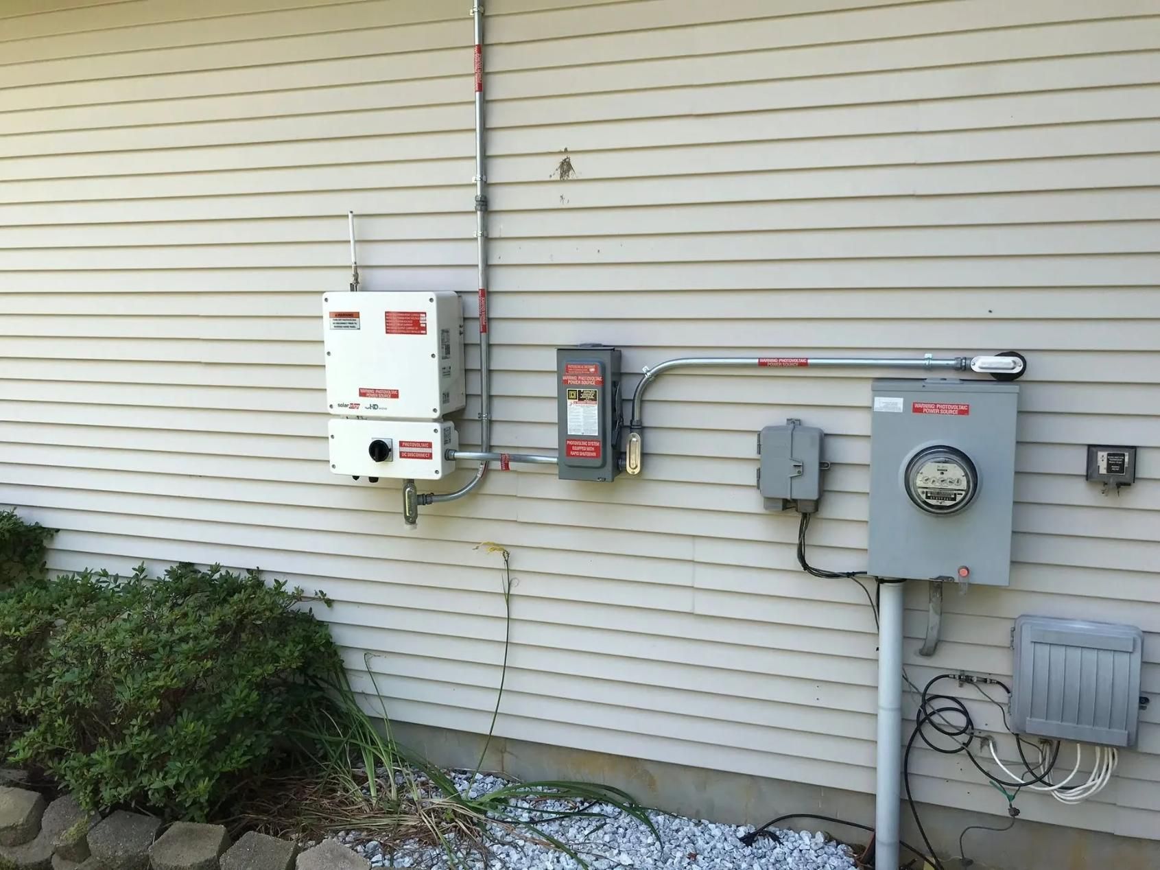 Exterior wall with solar panel equipment: inverter, disconnect, and meter box.