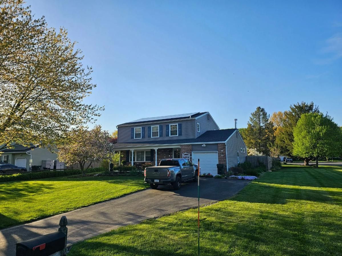 Two-story house with solar panels, driveway, and truck on a sunny day. 