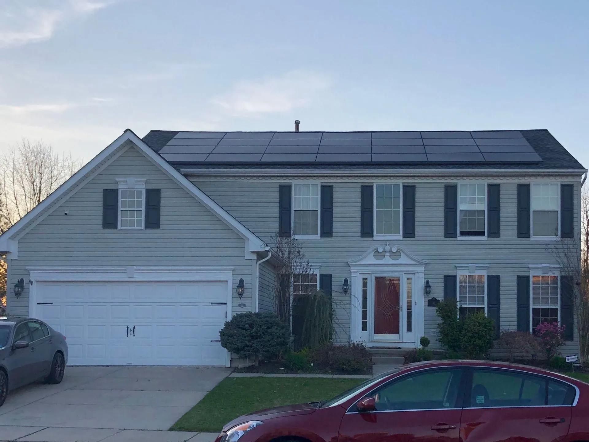 Two-story house with solar panels on the roof, light green siding, white garage door, and a red front door.