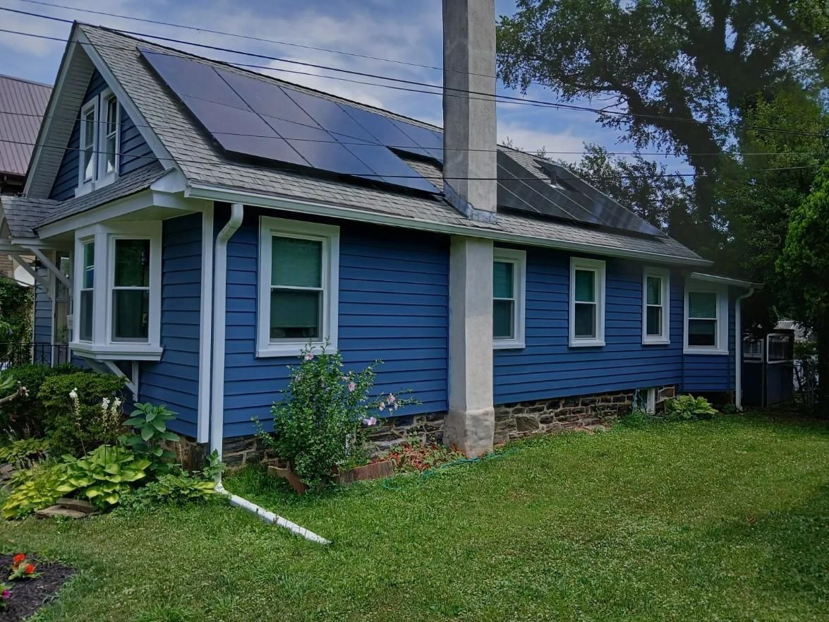 Blue house with solar panels on roof, green lawn, and plants.