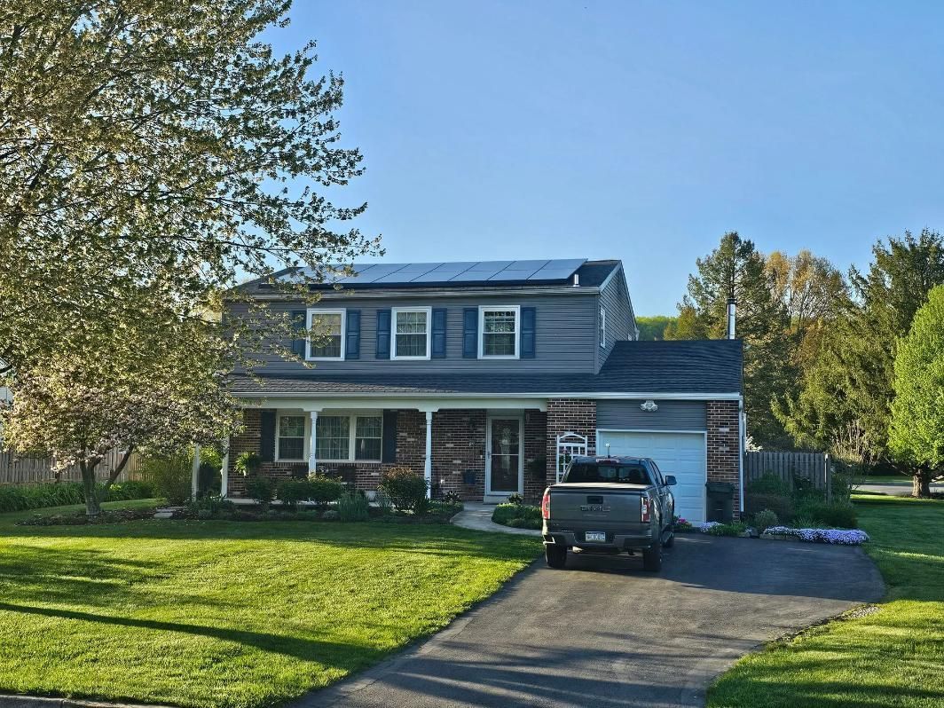 Blue house with solar panels on roof, shutters, and a driveway with a truck parked in front.