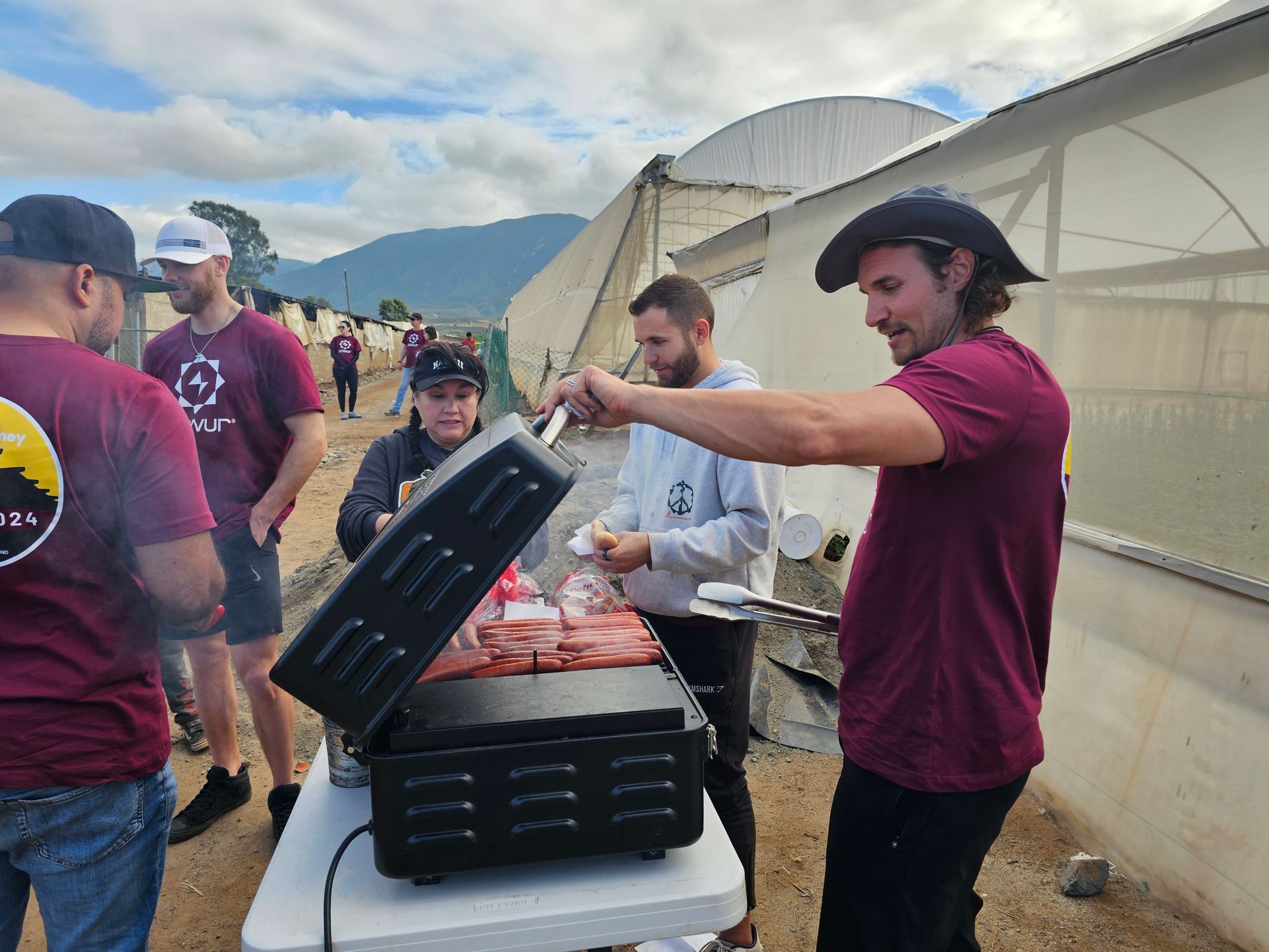 People serving food at an outdoor festival near tents and mountains