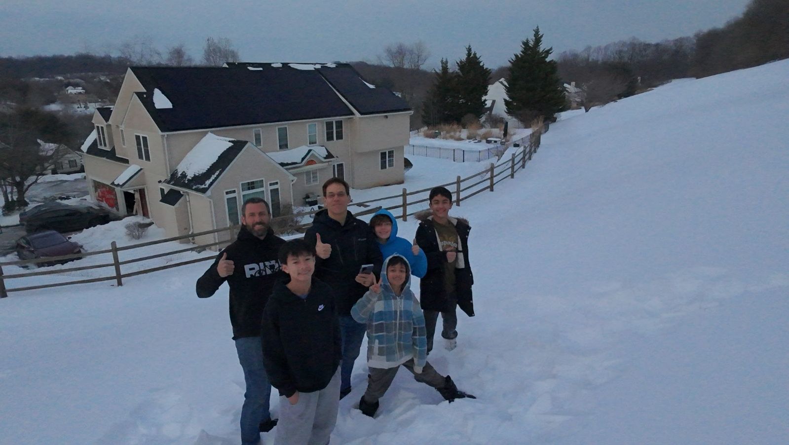 People posing on a snowy hillside near a house at dusk