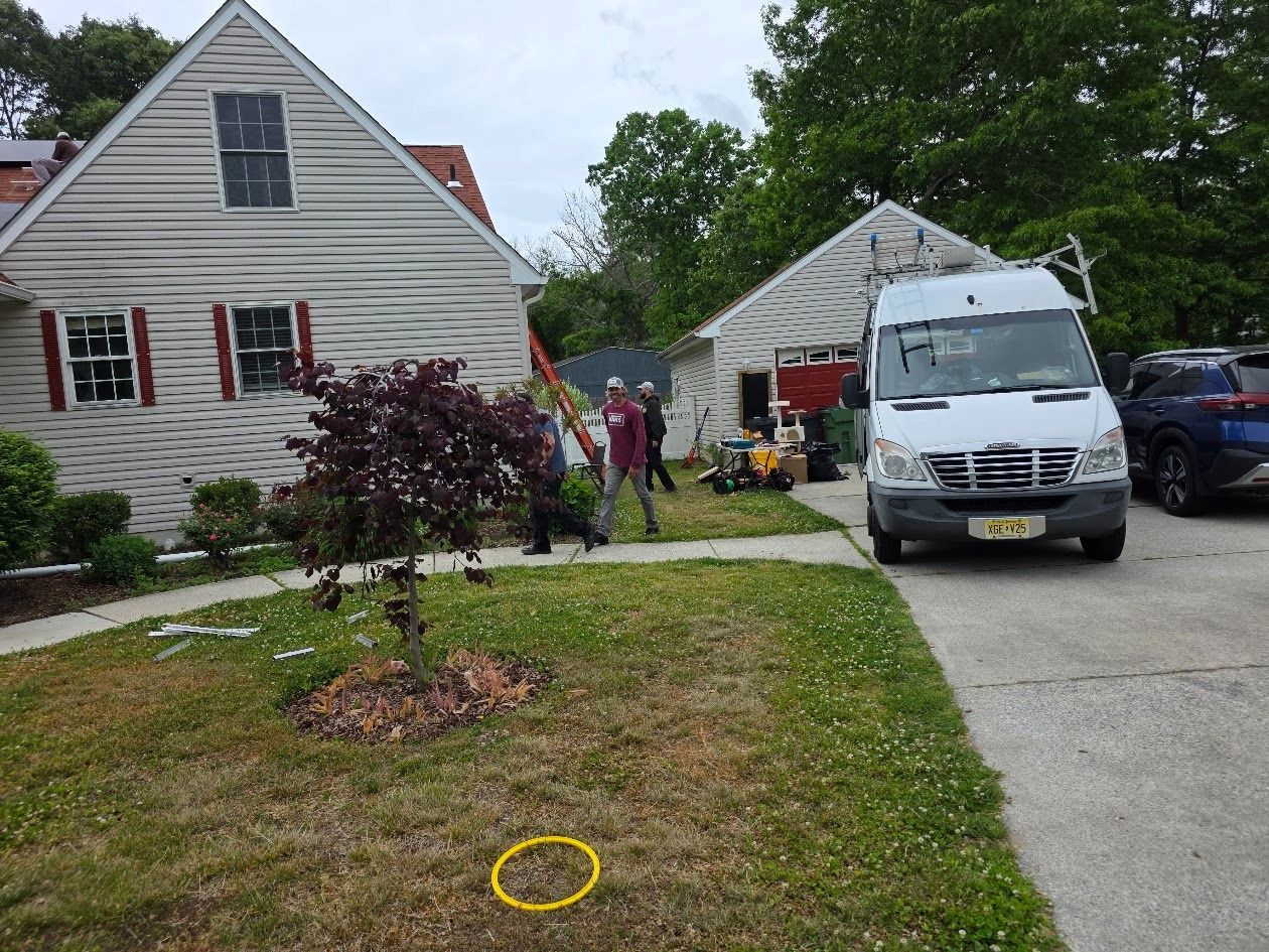 White van parked in a suburban driveway beside a house, with people near the garage and a small yard in front.
