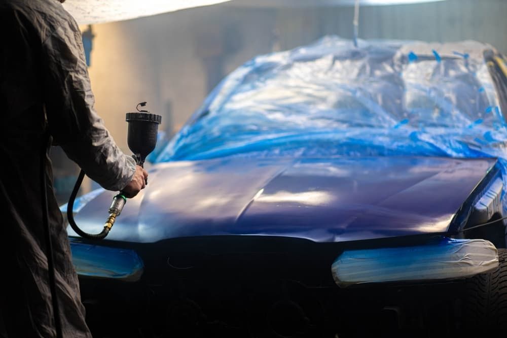 A Man Is Spray Painting a Purple Car in A Garage — Andy's A1 Auto Care in Barrack Heights, NSW