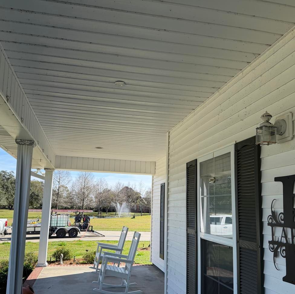White porch with white ceiling, siding, and pillars; two chairs, black shutters, and a lawn.