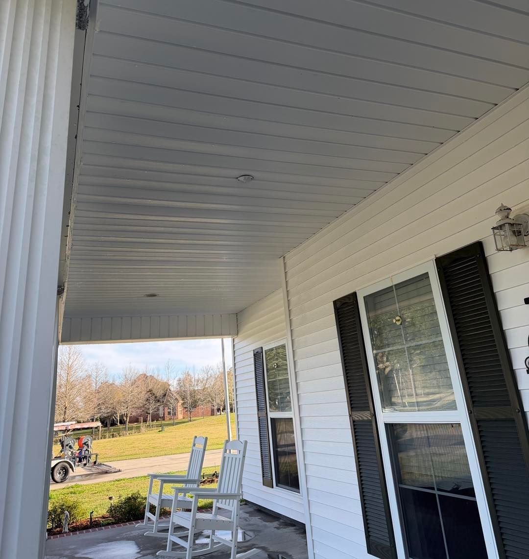 White porch ceiling and siding, black shutters, white chairs, yard in the background.