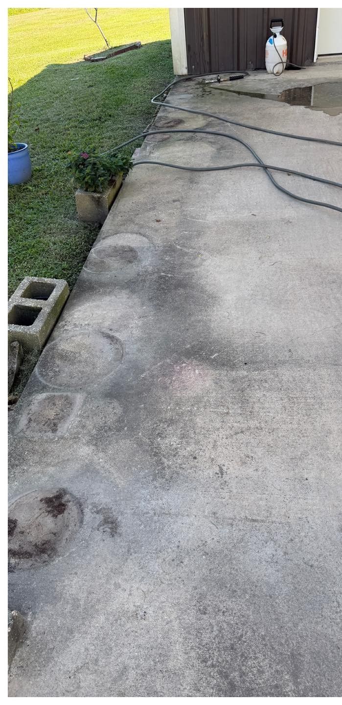 Concrete patio with a grassy lawn on the left and a building on the right. A hose runs across the patio.