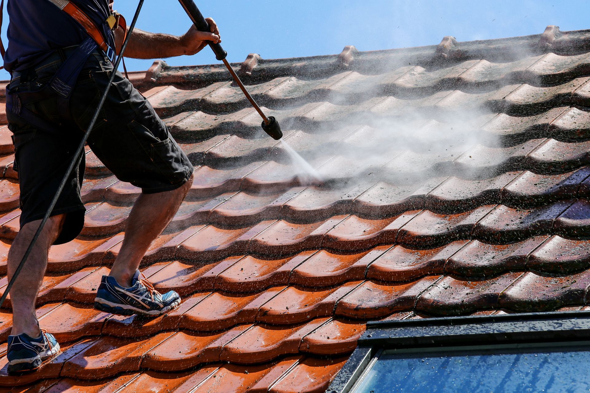 Person power washing a red tile roof with safety harness.