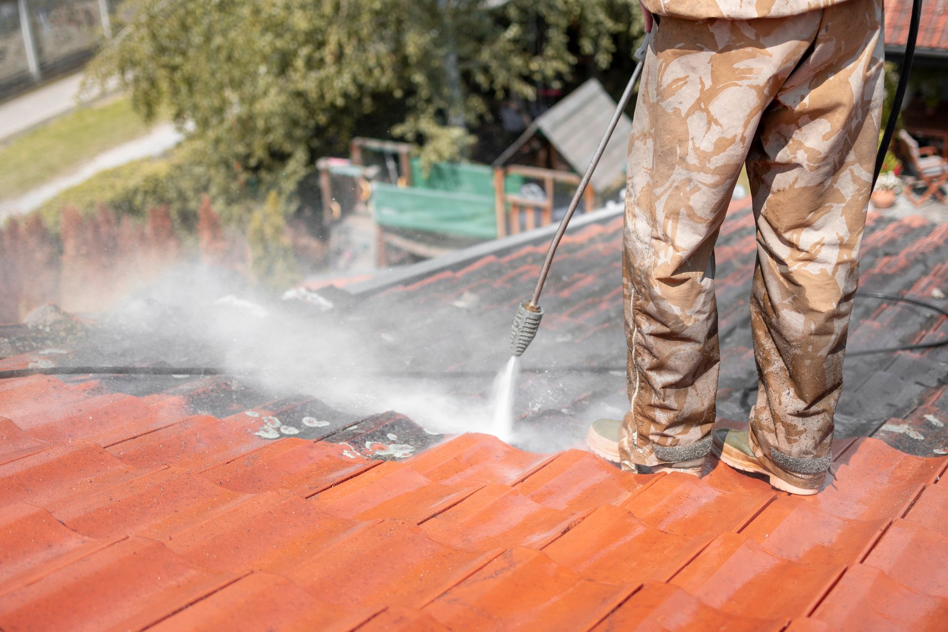 Person power washing a red tiled roof; outdoors, daytime.
