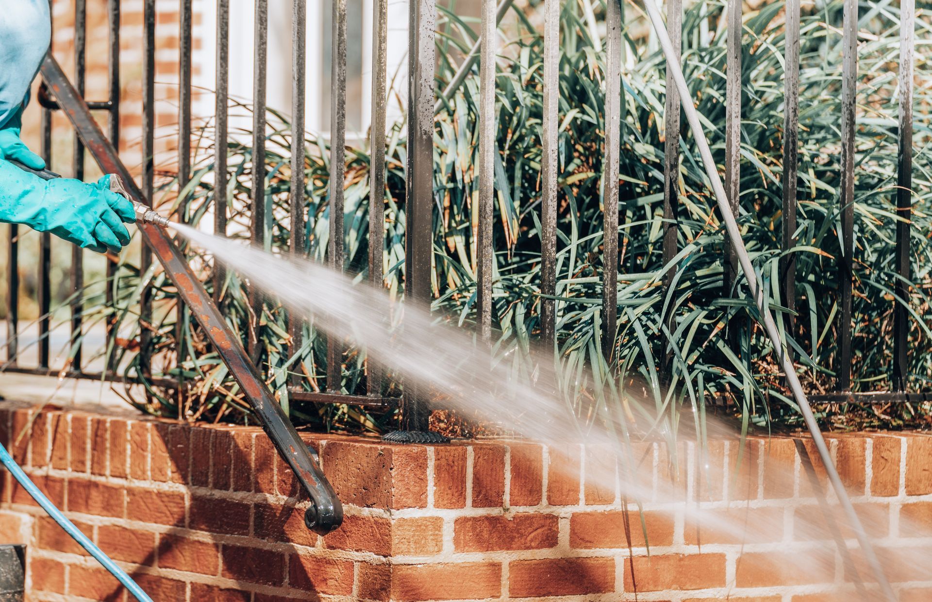 Person in blue gloves power washing a brick wall and metal railing.