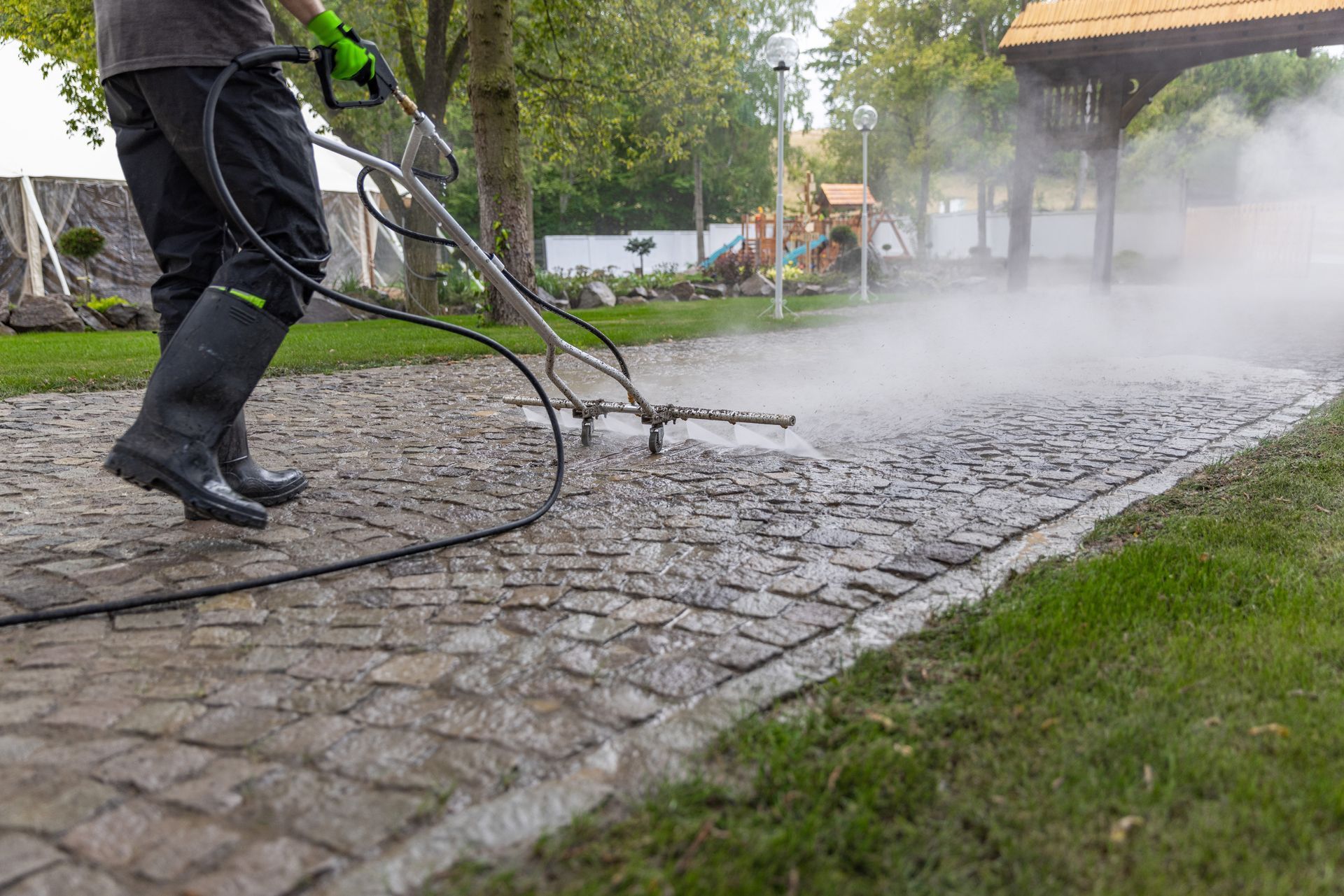 Person power washing a cobblestone walkway outdoors, creating steam.