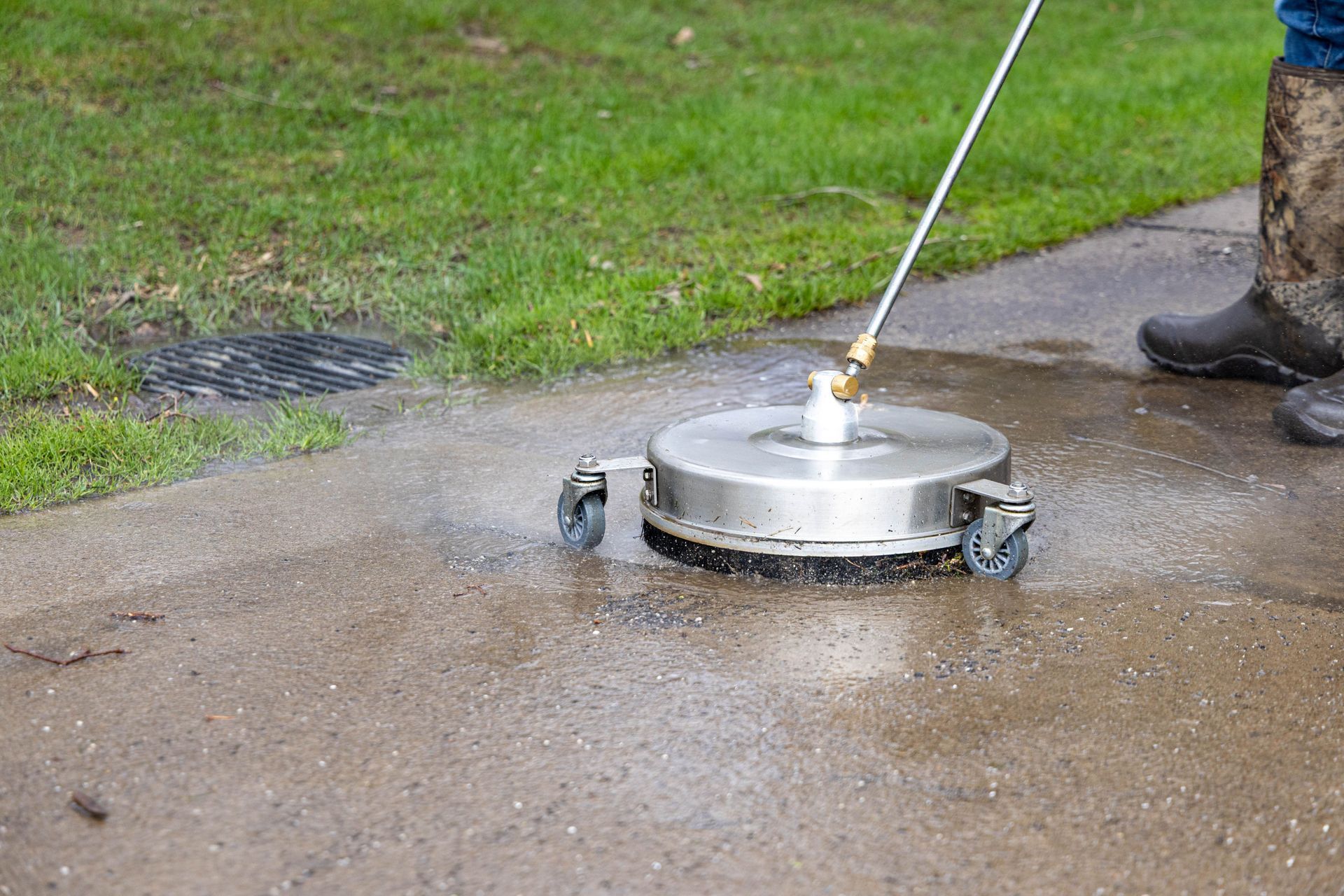 Person using a surface cleaner on a concrete sidewalk near grass.