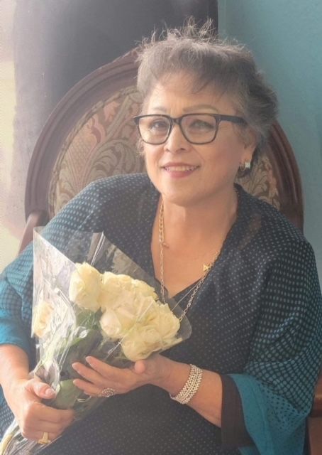 A woman wearing glasses is sitting in a chair holding a bouquet of white roses.