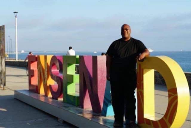 A man stands in front of a sign that says ensenada