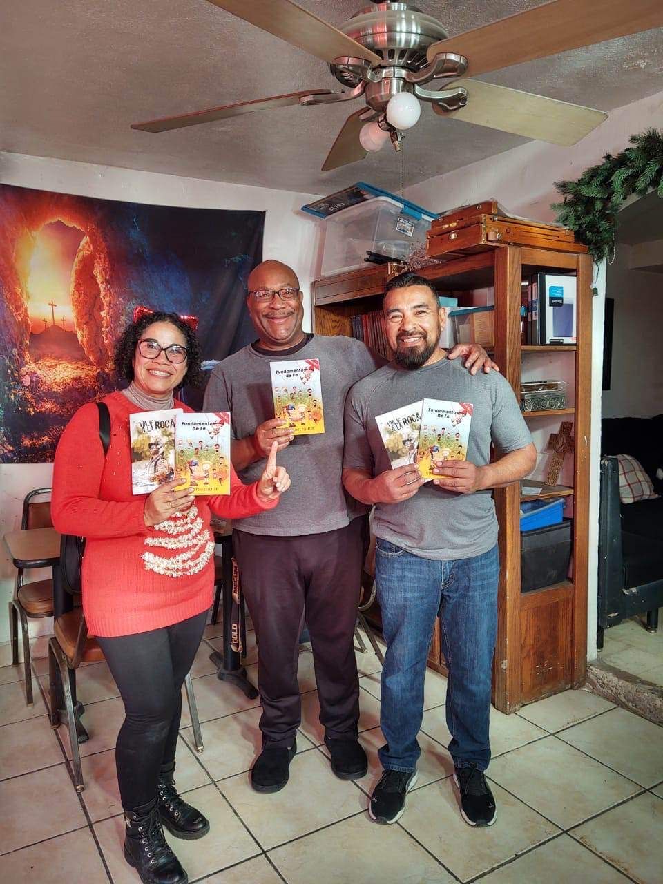 Three people are standing in a living room holding books.