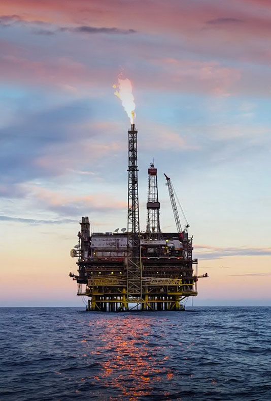 an oil rig in the middle of the ocean at sunset .