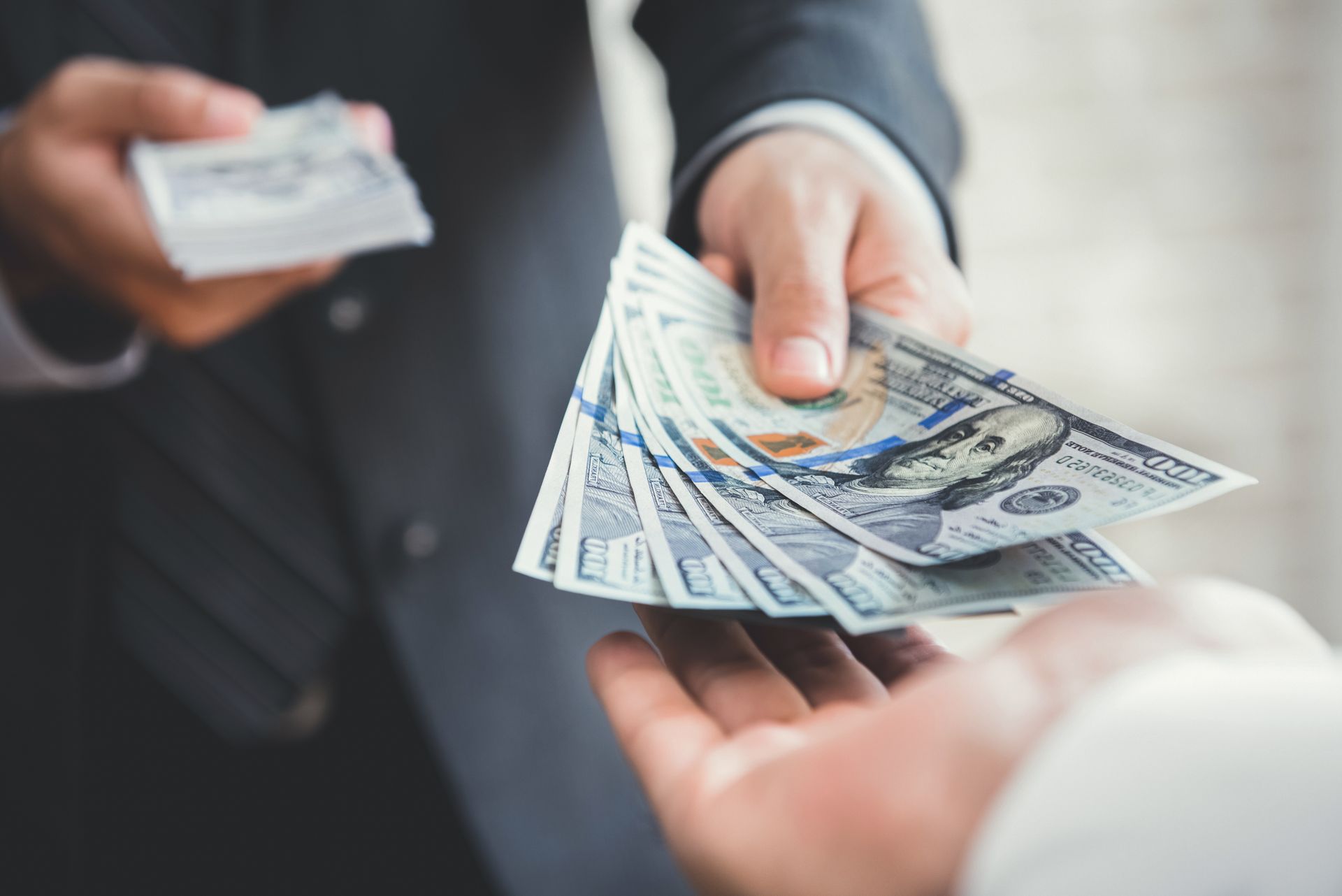 Close-up of hands exchanging a stack of hundred-dollar bills during a cash transaction.