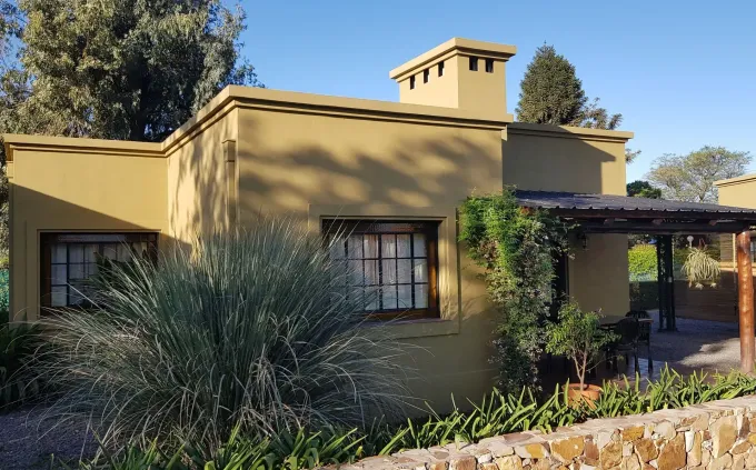 Casa amarilla de estuco con porche delantero, chimenea y paisajismo desértico bajo un sol radiante