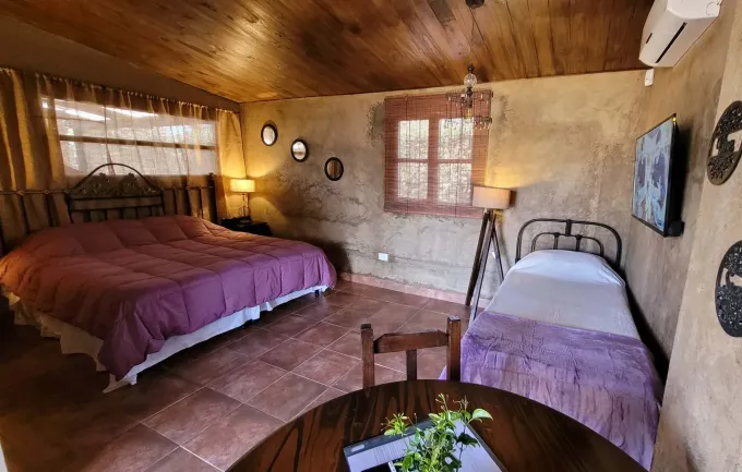 Dormitorio rústico con dos camas, techo de madera, suelo de terracota y una pequeña mesa redonda con flores
