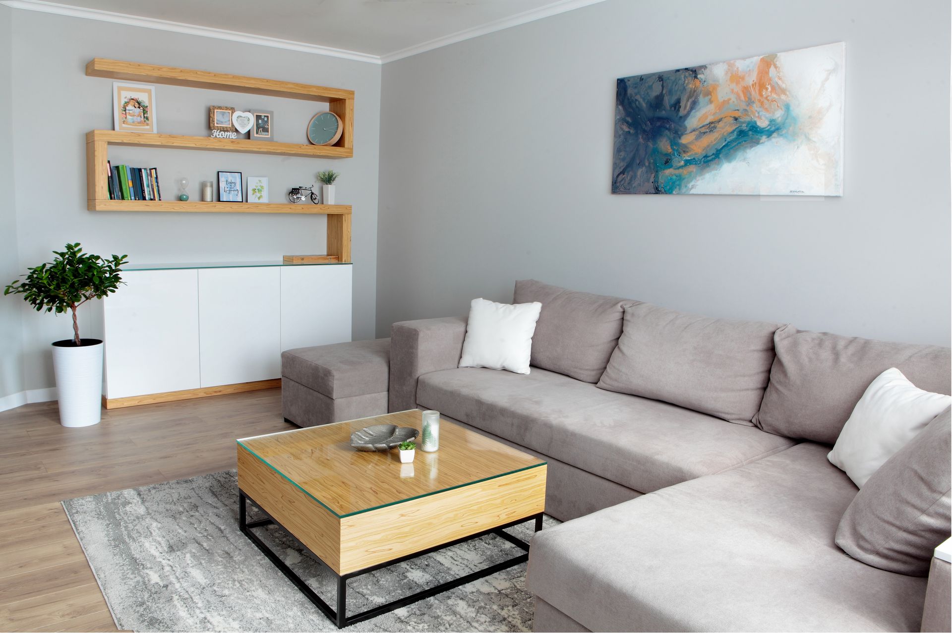 Modern living room with gray sectional, wooden coffee table, wall art, and floating shelves