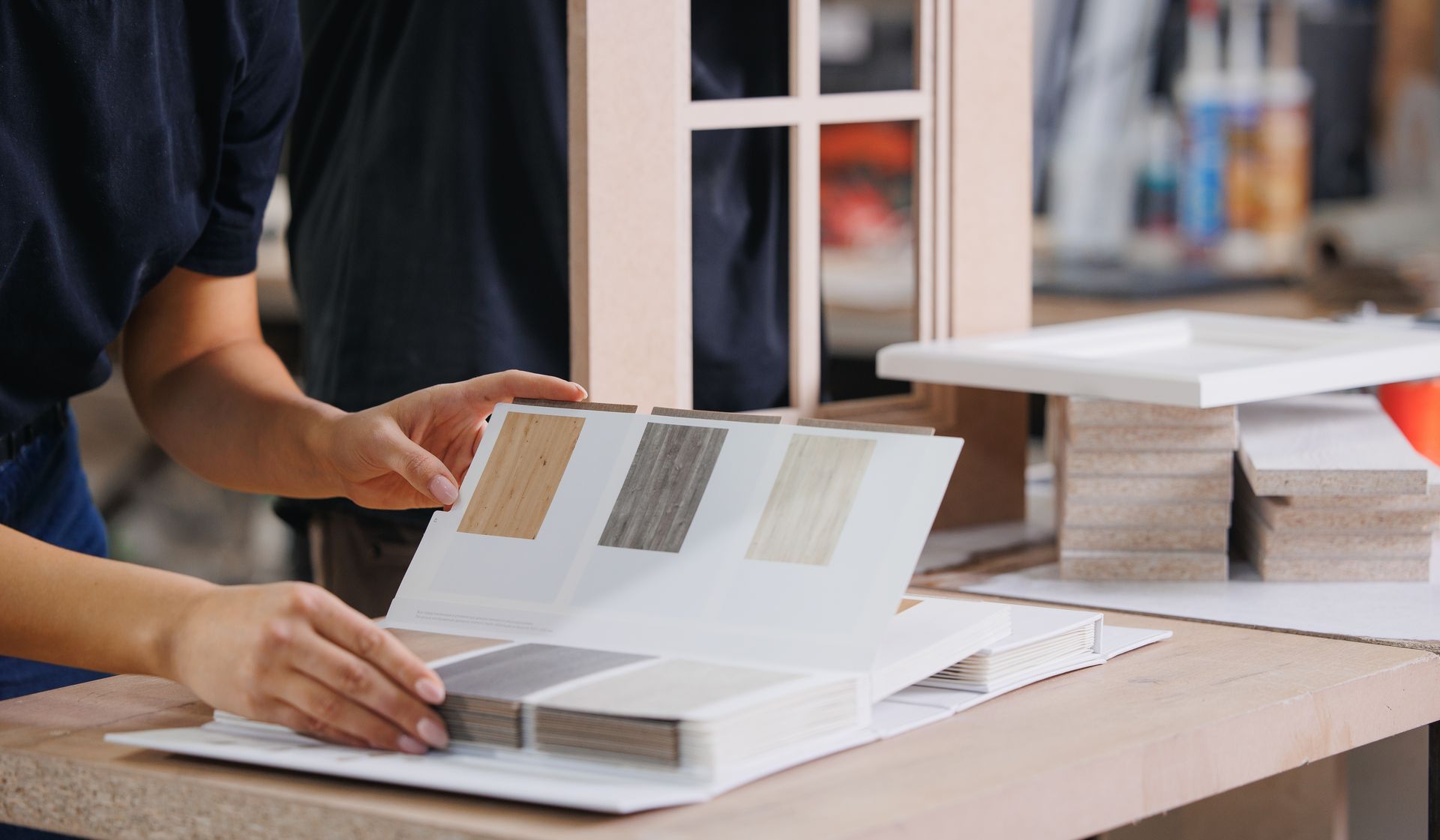 Person flipping through open design catalogues at a desk in a bright office.