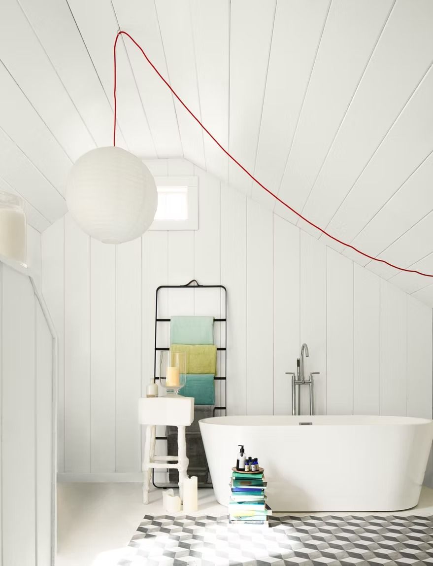 Bright white bathroom with freestanding tub, round pendant light, mirror, and red cord on slanted ceiling.