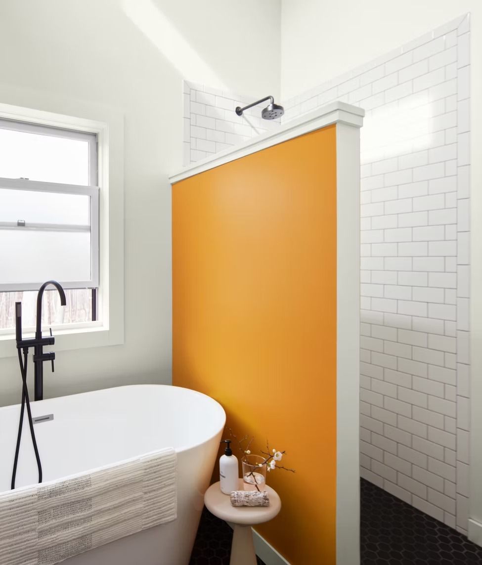 Bright bathroom with orange shower wall, white subway tile, bathtub, and window.