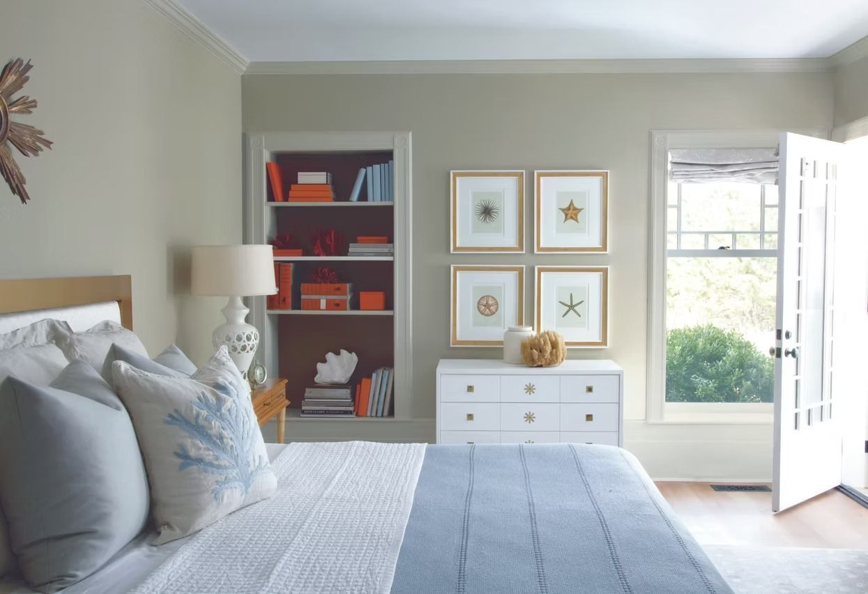 Bright bedroom with blue bed, white dresser, bookshelf wall art, and an open door to the outside.