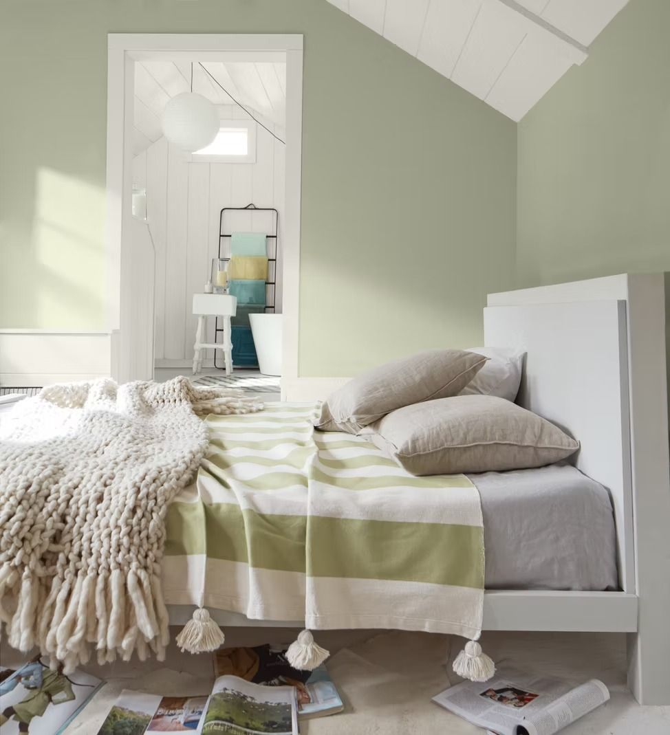 Cozy bedroom with pale green walls, white bedframe, striped blanket, and fuzzy throw by a window seat
