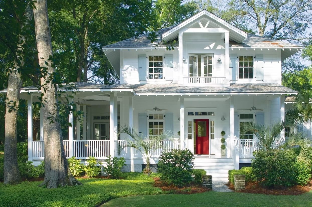White two-story house with a red front door, white porch, and lush green lawn in a wooded setting