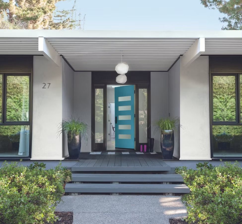 Modern house entry with teal front door, steps, and potted plants under a covered porch