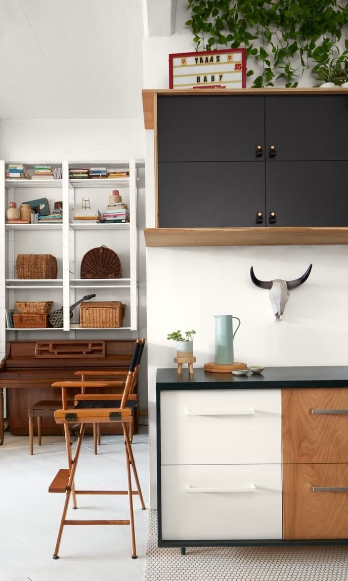 Modern kitchen with black cabinets, white shelving, and wooden stools beside a compact counter.