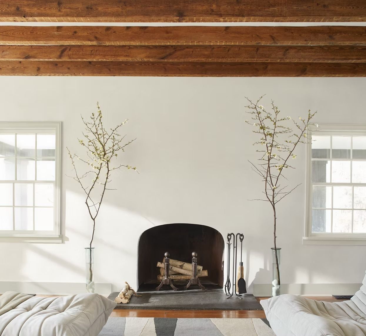 Minimal white living room with exposed wood ceiling, fireplace, and two bare branch arrangements