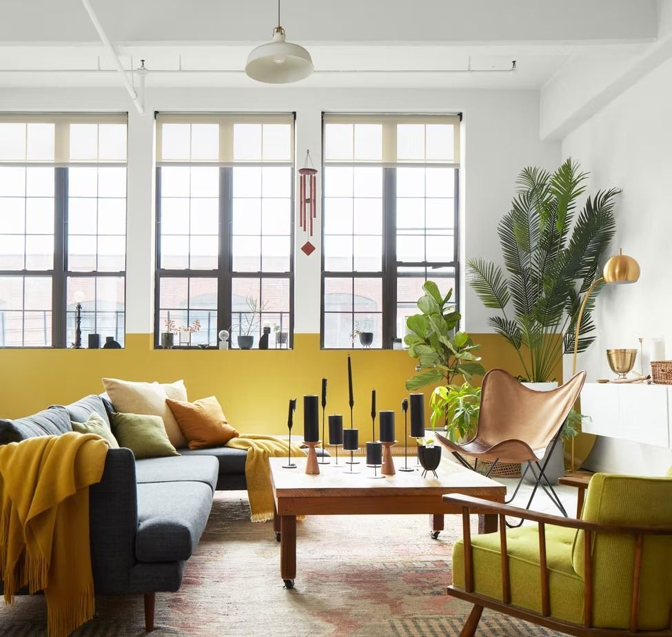 Bright living room with yellow sofa, wood coffee table, plants, and large windows with black frames