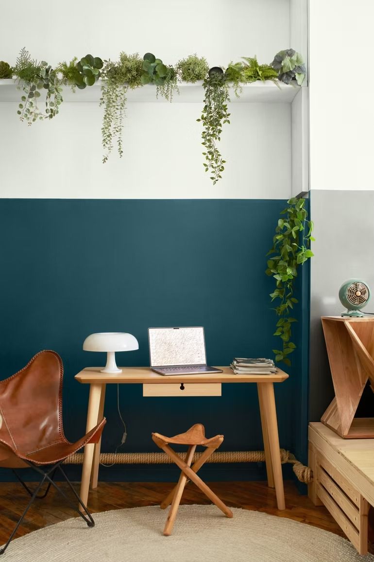Modern home office nook with teal wall, wooden desk, chair, and hanging plants
