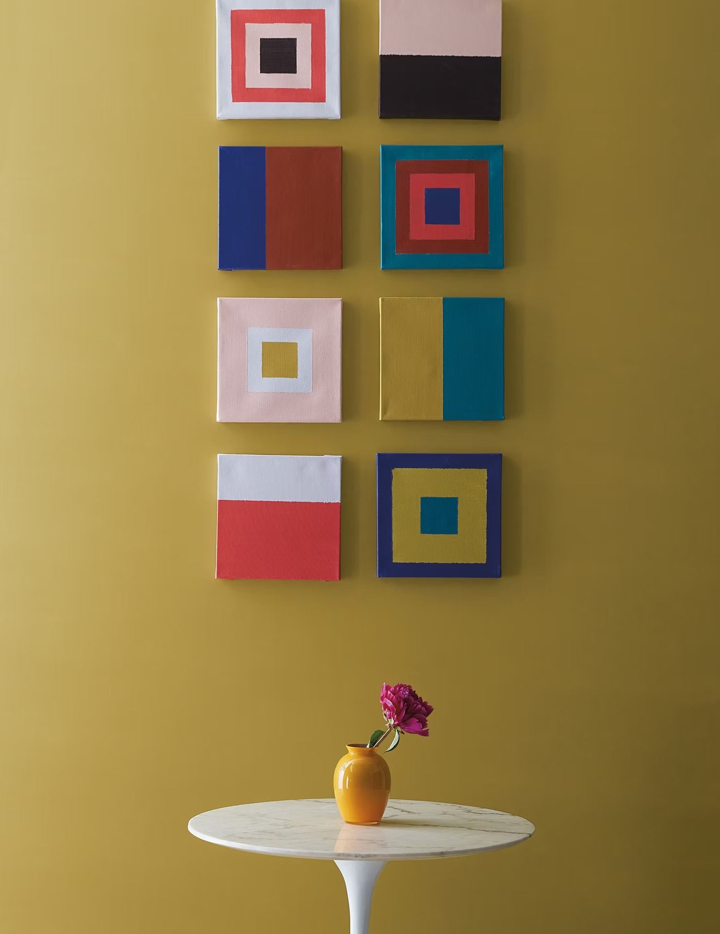 Colorful abstract wall art above a small round table with a vase of flowers on a yellow wall.