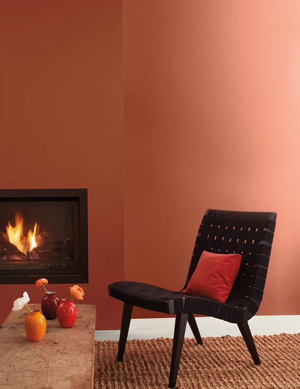 Modern living room with a black chair, red pillow, and fireplace against a terracotta wall