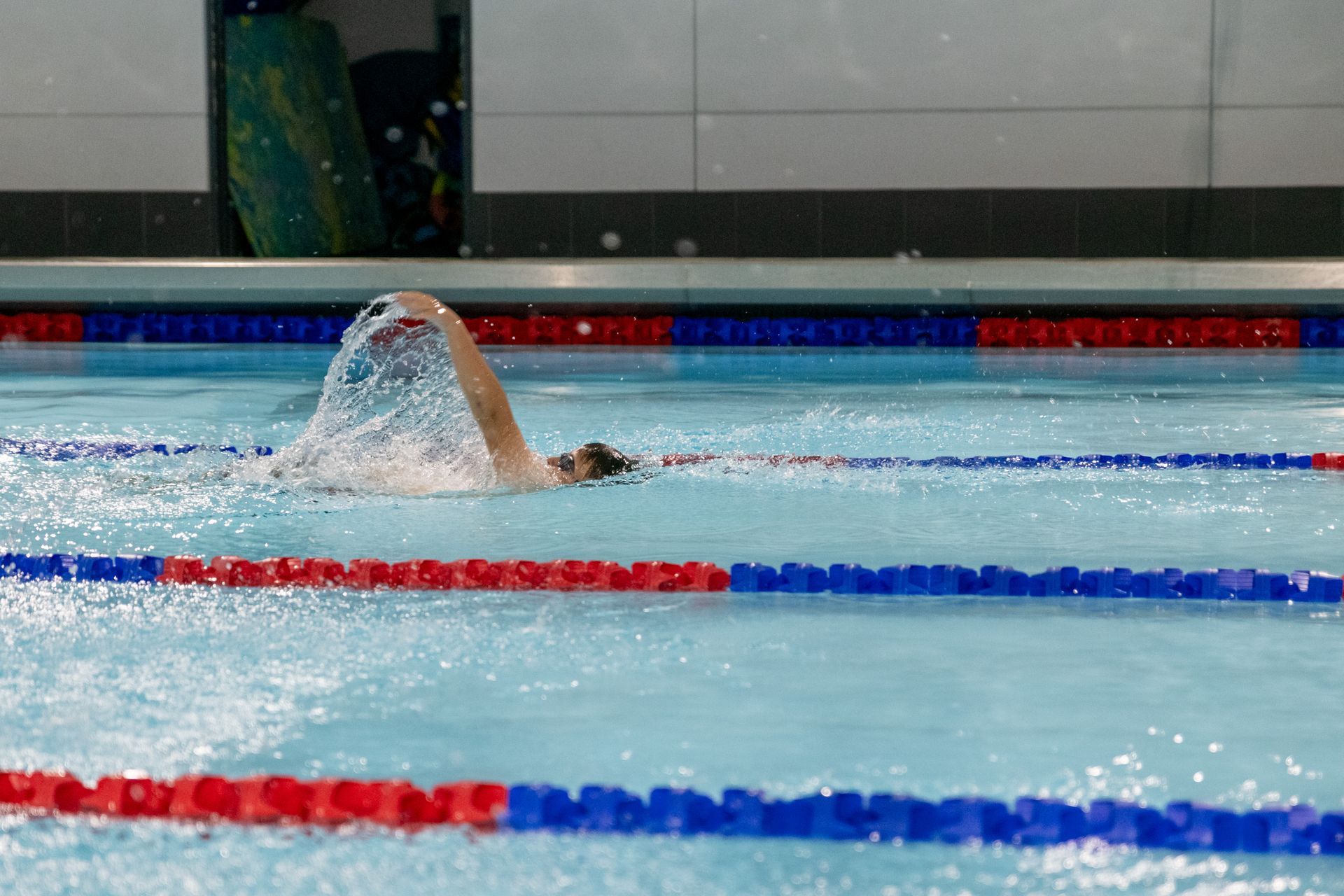 A person is swimming in a swimming pool with red , white and blue lanes.
