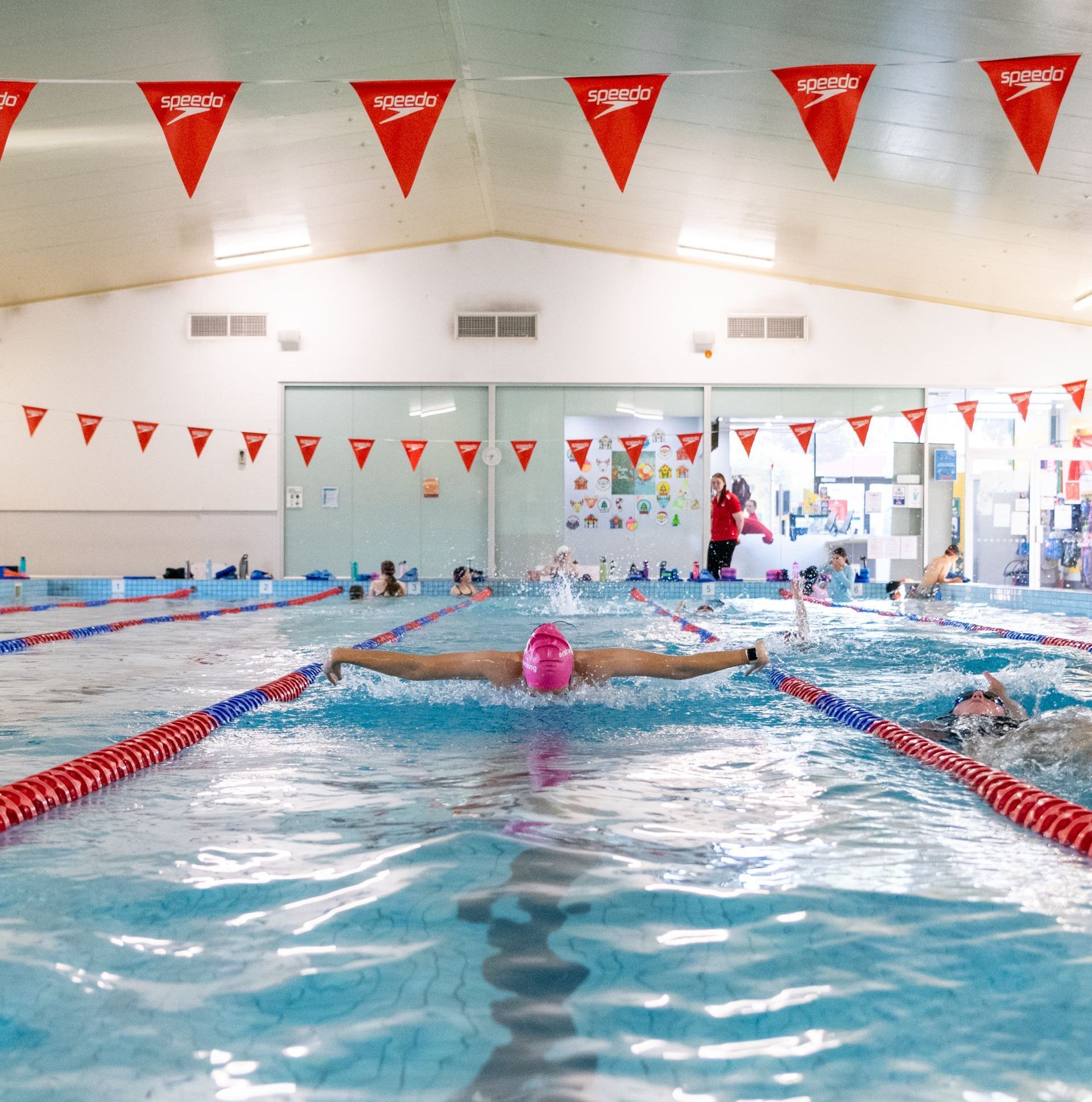 A woman is swimming in a pool with speedo flags hanging from the ceiling
