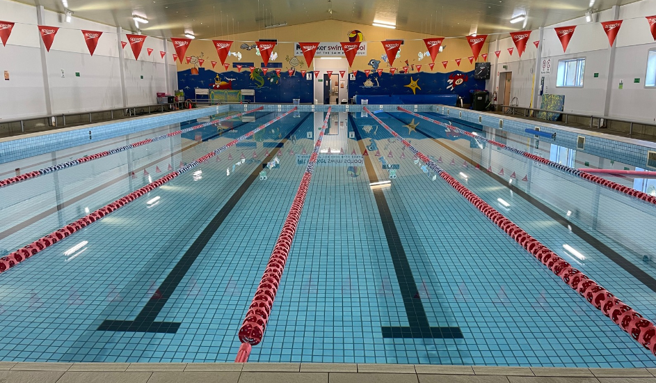 A large indoor swimming pool with red lanes and flags hanging from the ceiling.