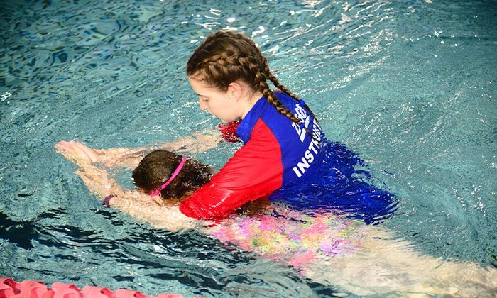 A woman is teaching a young girl how to swim in a swimming pool.