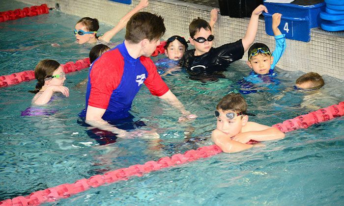 A man is teaching a group of children how to swim in a swimming pool.