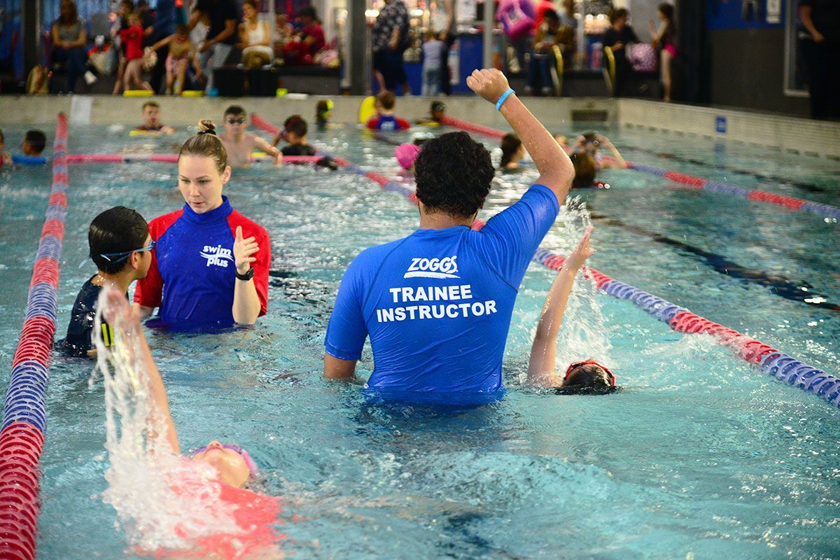 A man in a blue shirt that says trainer instructor is swimming in a pool.