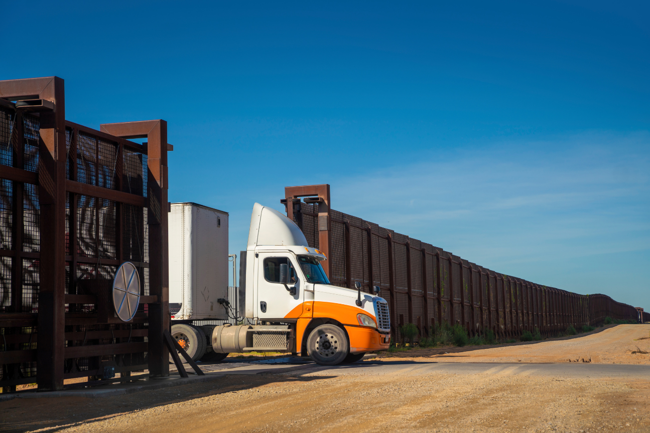 A semi truck is parked next to a fence on a dirt road.