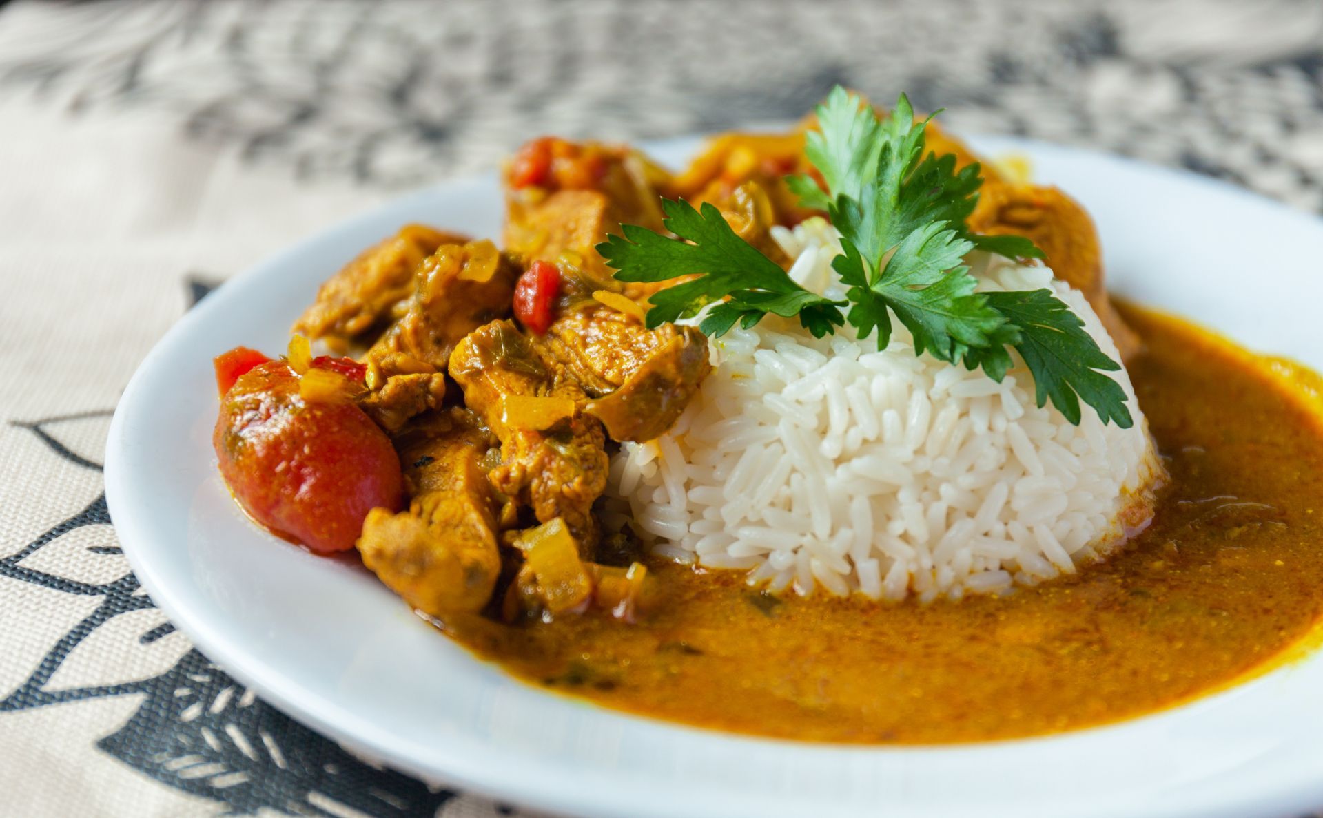 Curry with rice on a white plate, garnished with cilantro and cherry tomatoes