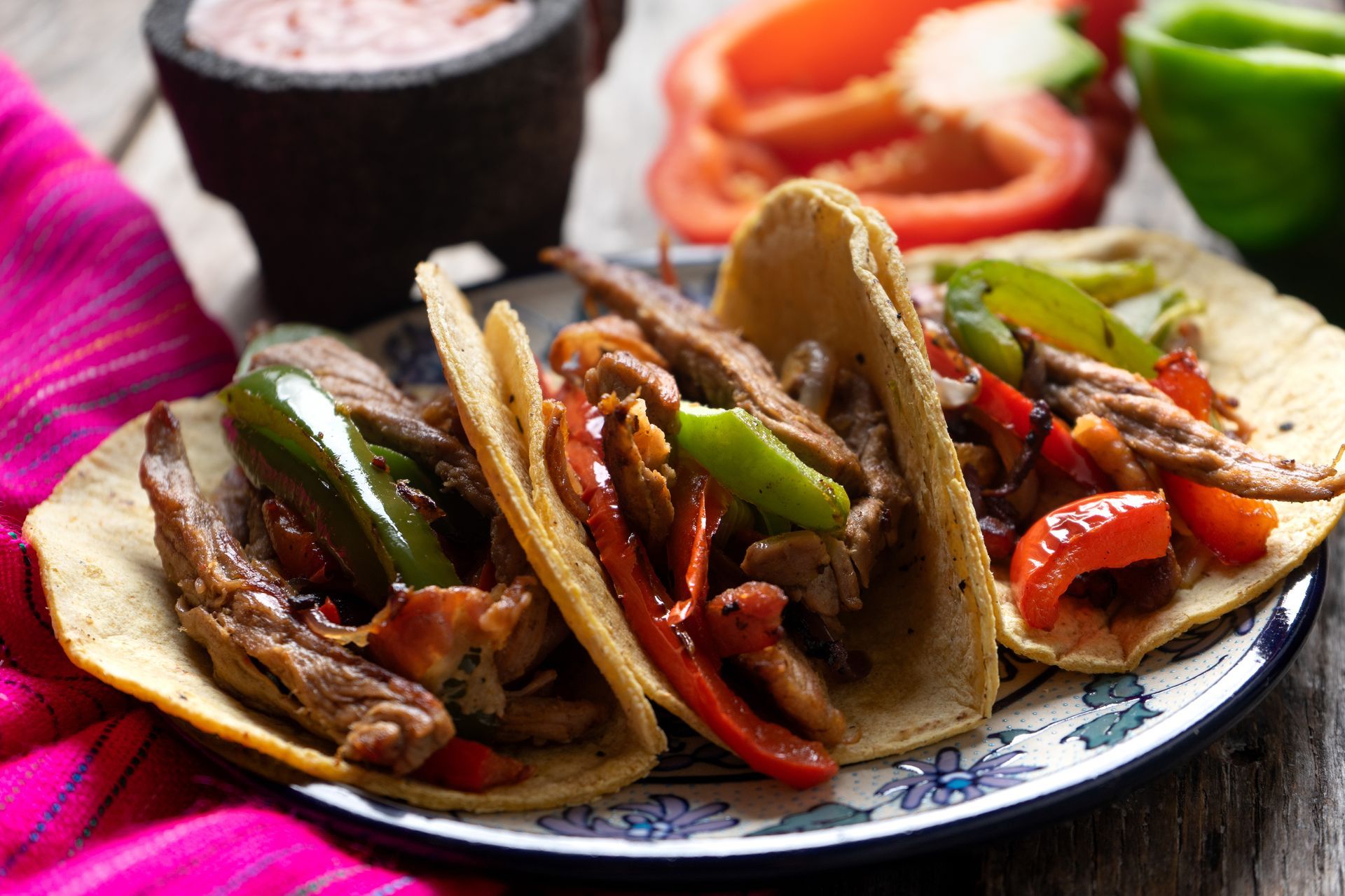Three beef tacos with peppers and onions on a plate, with salsa and rice in the background