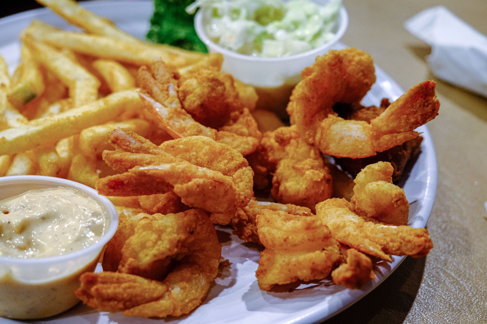 Plate of fried shrimp with French fries and dipping sauces on a table
