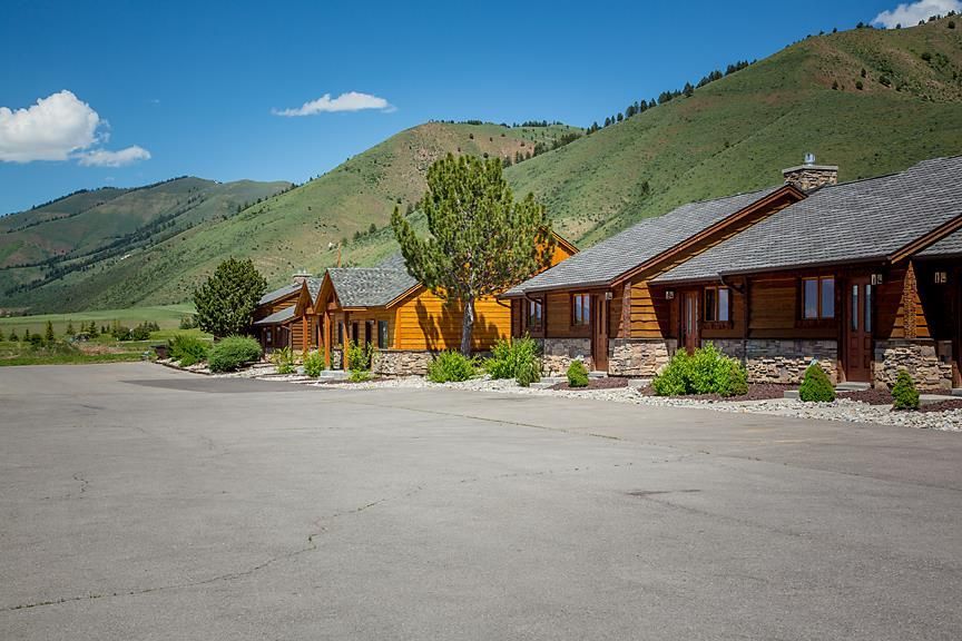 Wooden cabins along a paved road with green mountains under a blue sky
