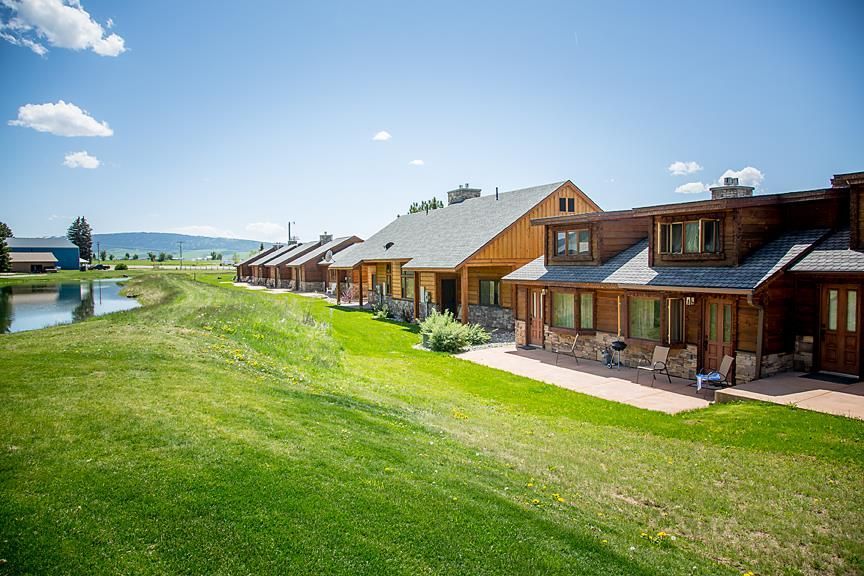 Row of rustic cabins beside a green lawn and pool under a bright blue sky